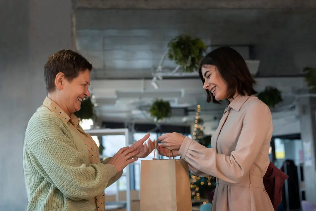 une femme donne un paquet à une autre salariée. les 2 personnes sourient, dans le cadre de la conciergerie d'entreprise gérée par EA HPF et Merci Oscar